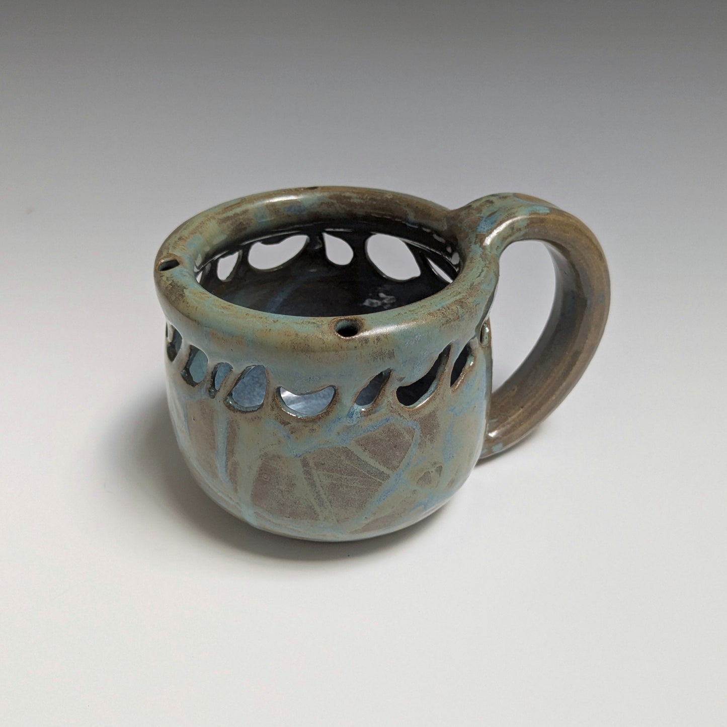 Ceramic mug with decorative holes on a gray background