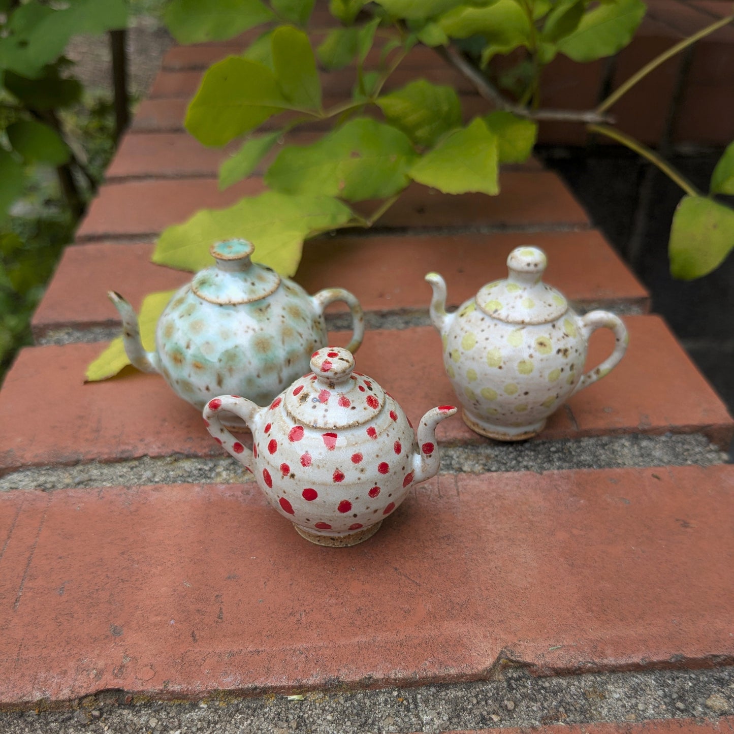 Three ceramic teapots with decorative dots on a brick surface.