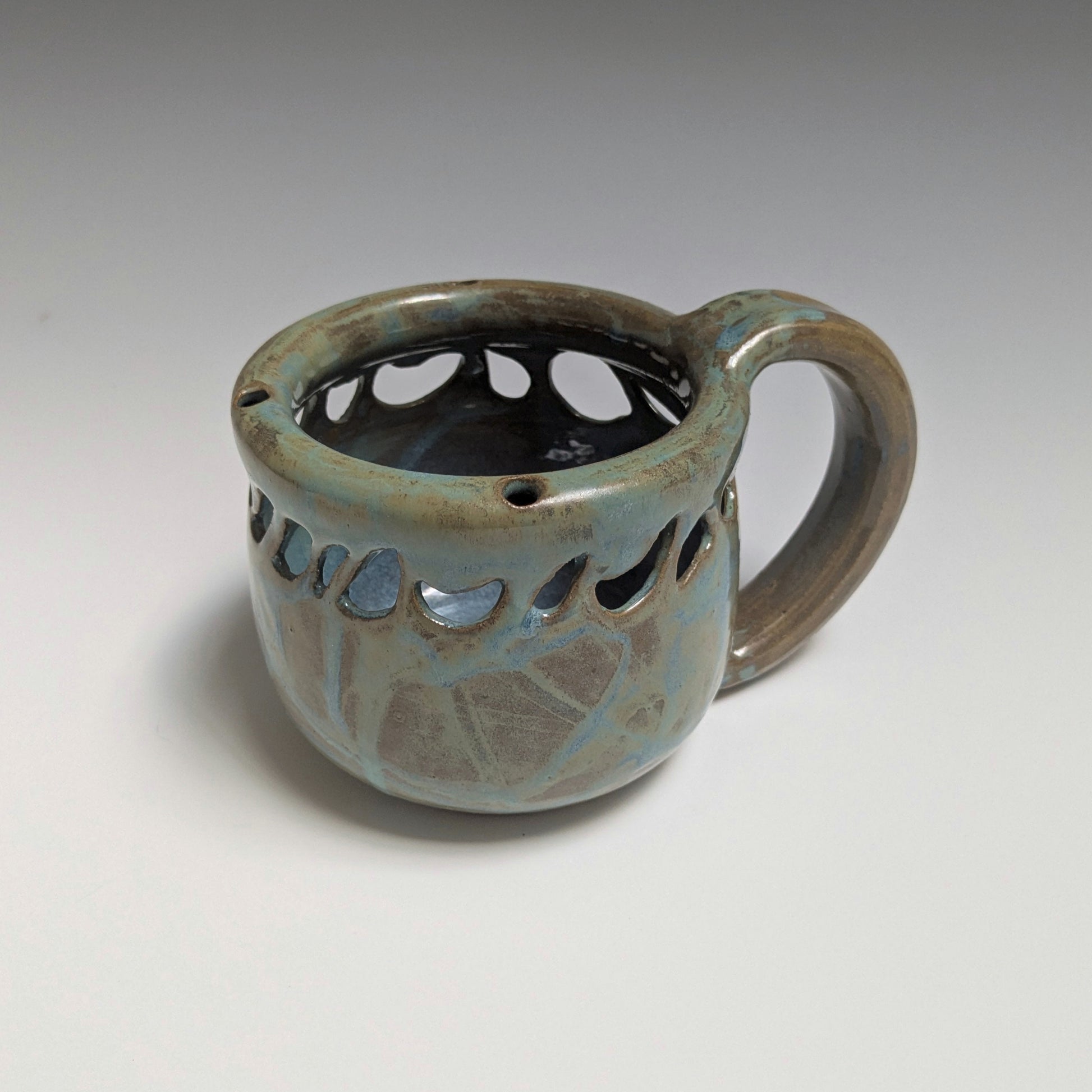 Ceramic mug with decorative holes on a gray background