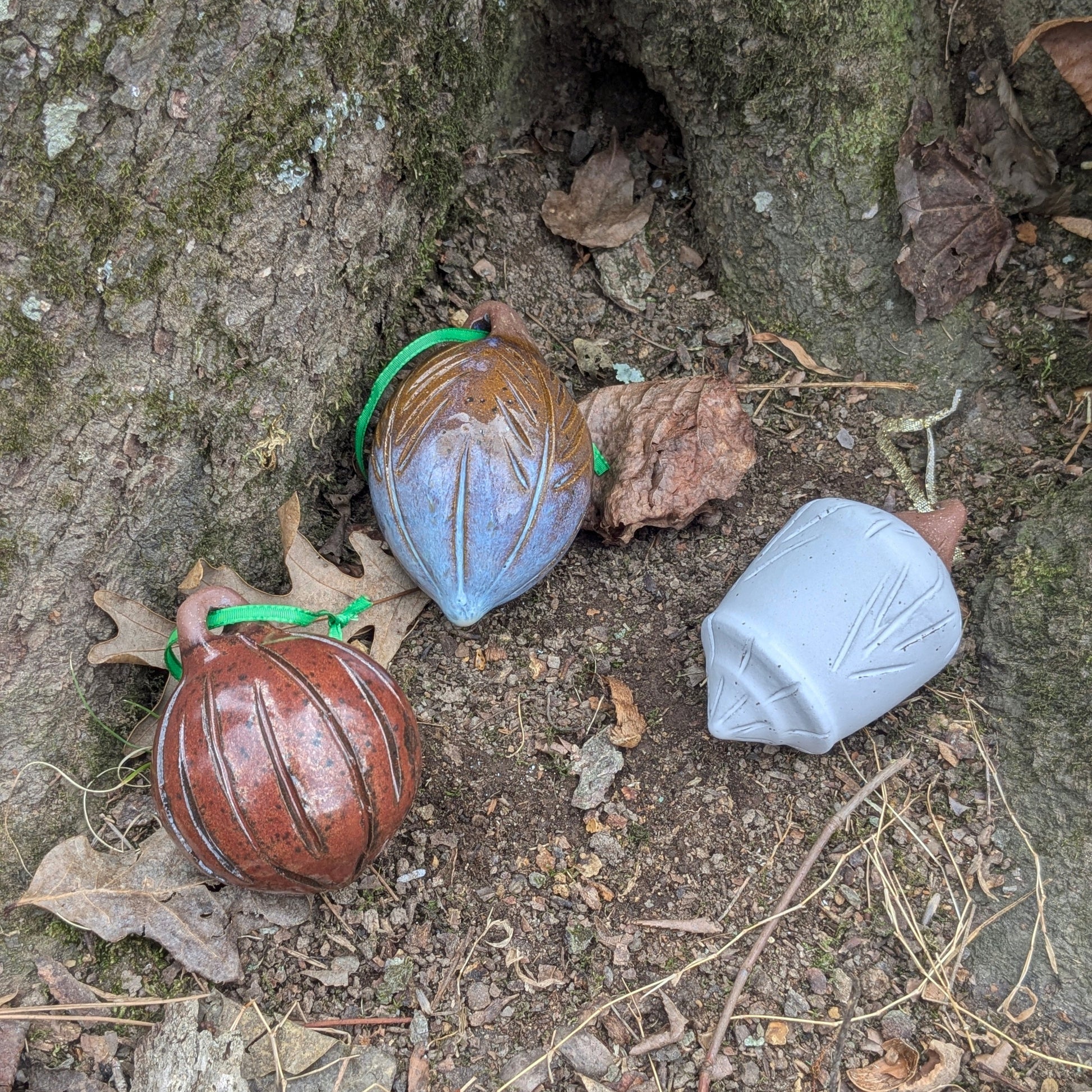 Three ornaments one red, one blue, and one white, on a tree trunk with leaves and twigs.