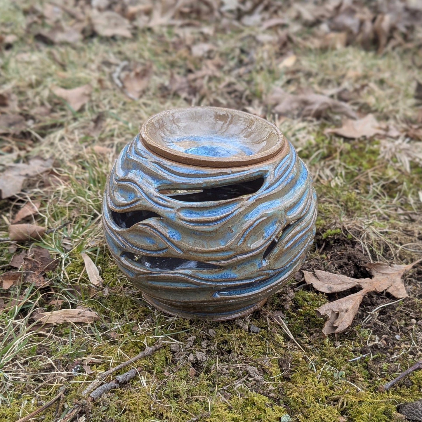 Ceramic vase with wavy design on a natural ground with grass and leaves