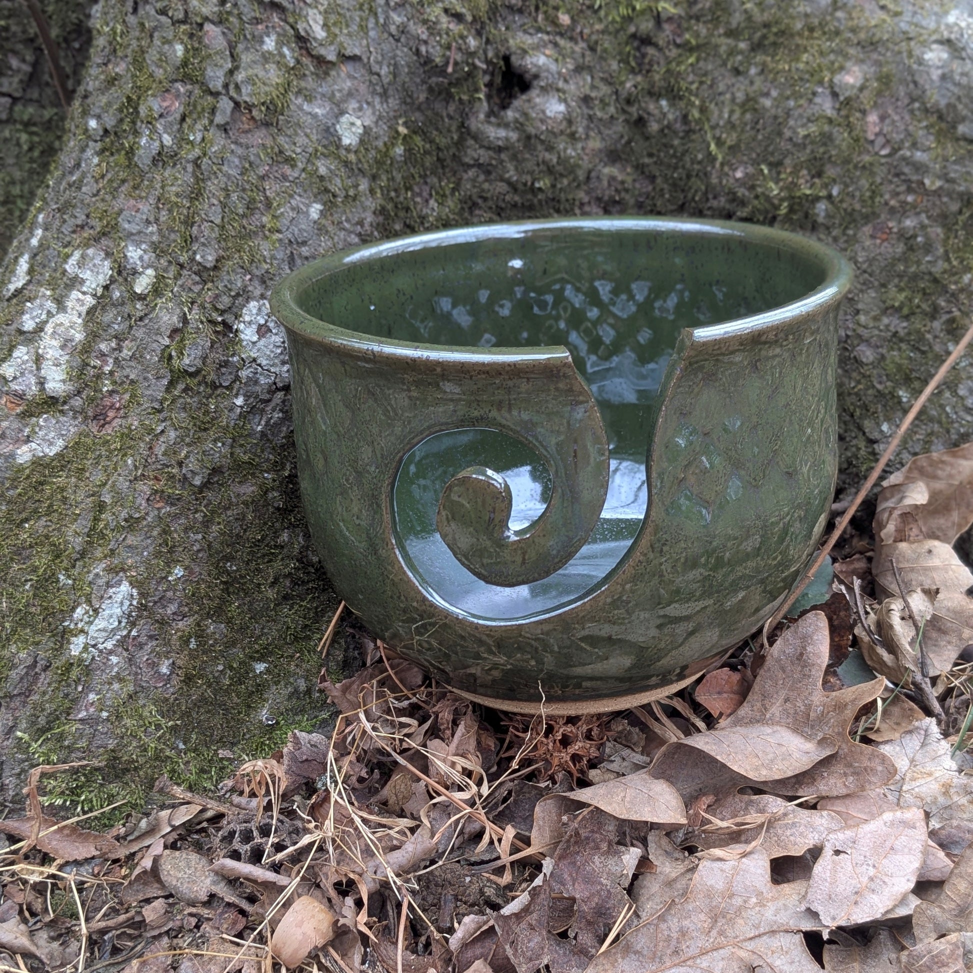 Green ceramic yarn bowl with a spiral design on a forest floor