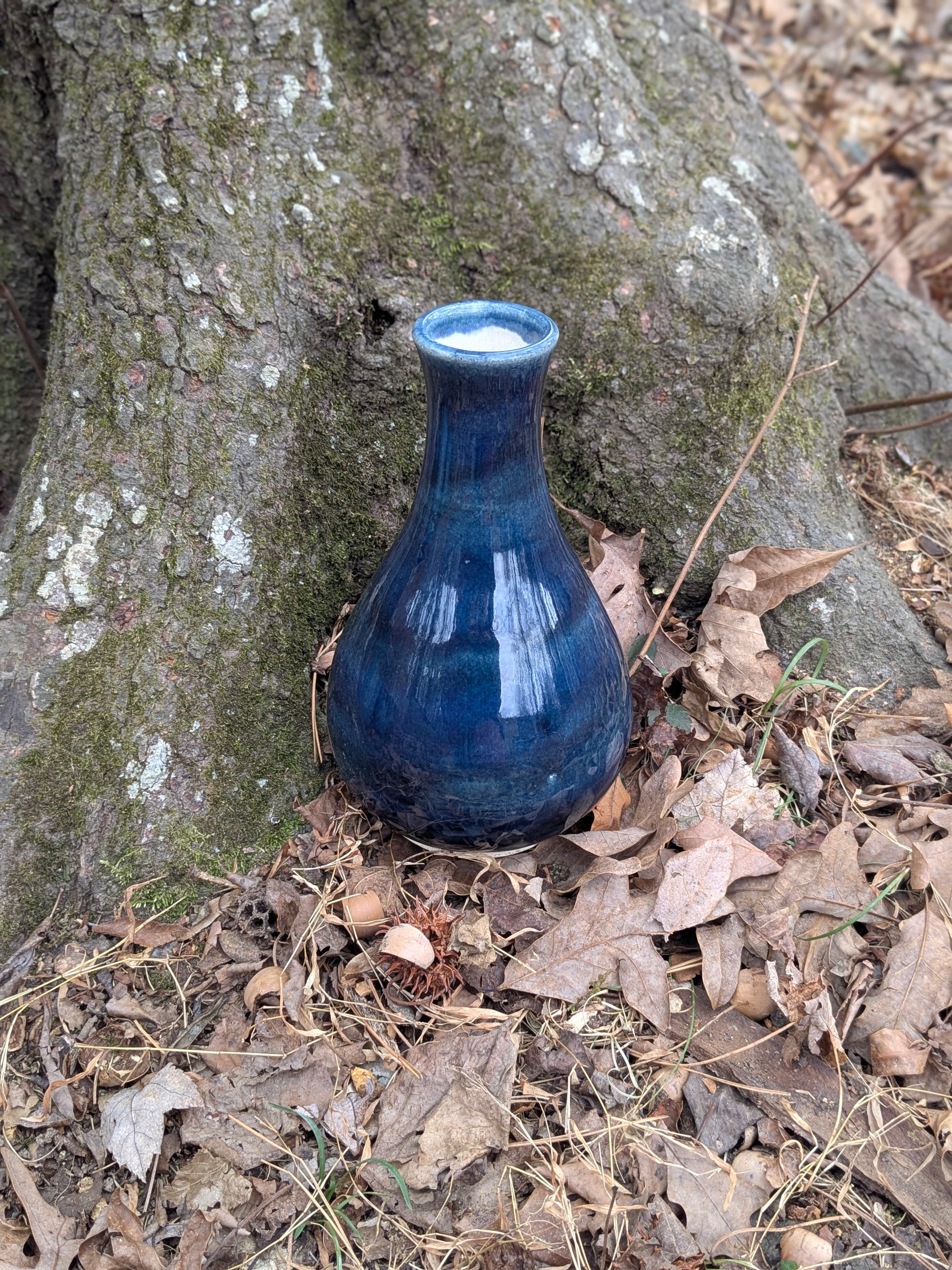Blue ceramic vase on the ground next to a tree