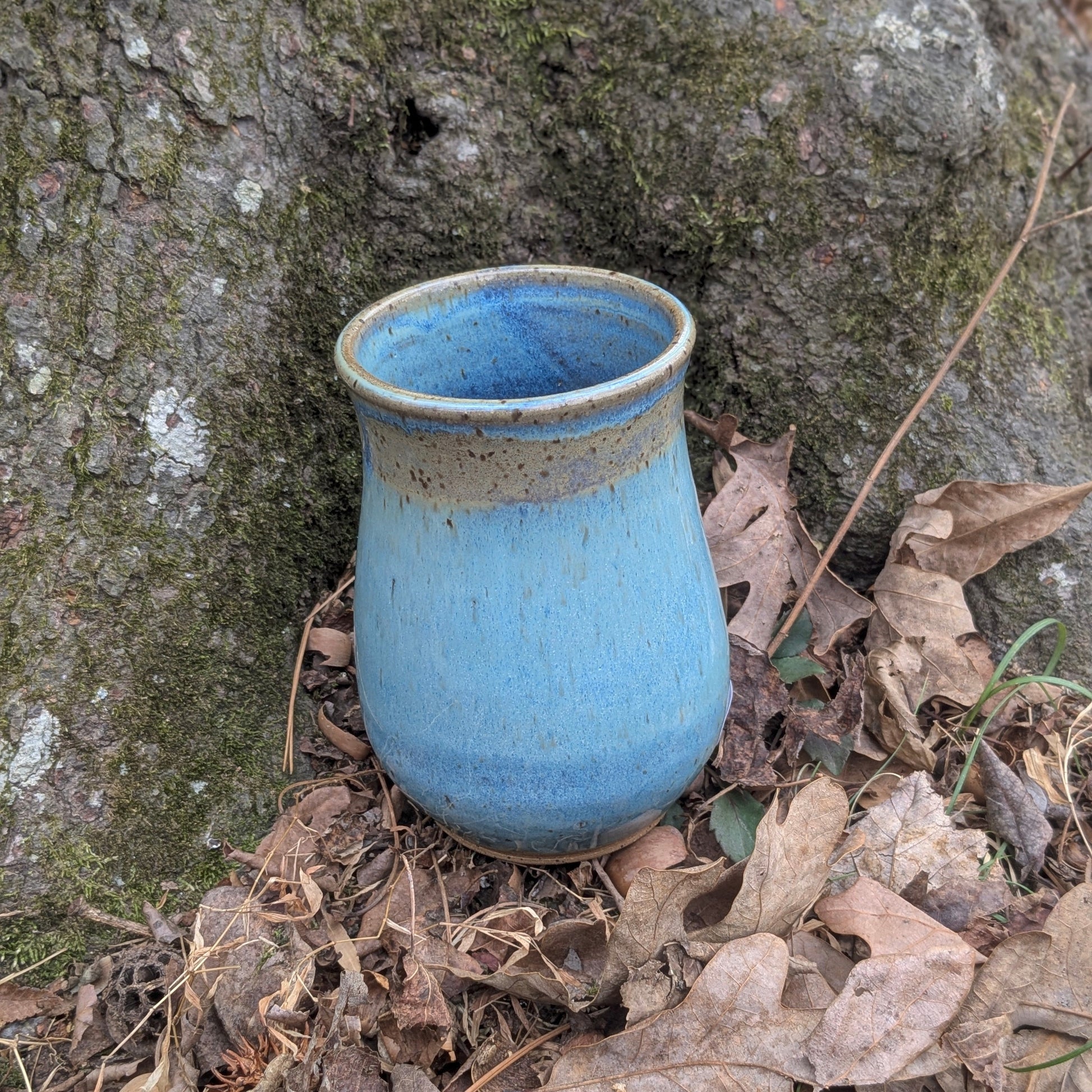 Blue ceramic vase on the ground next to a tree