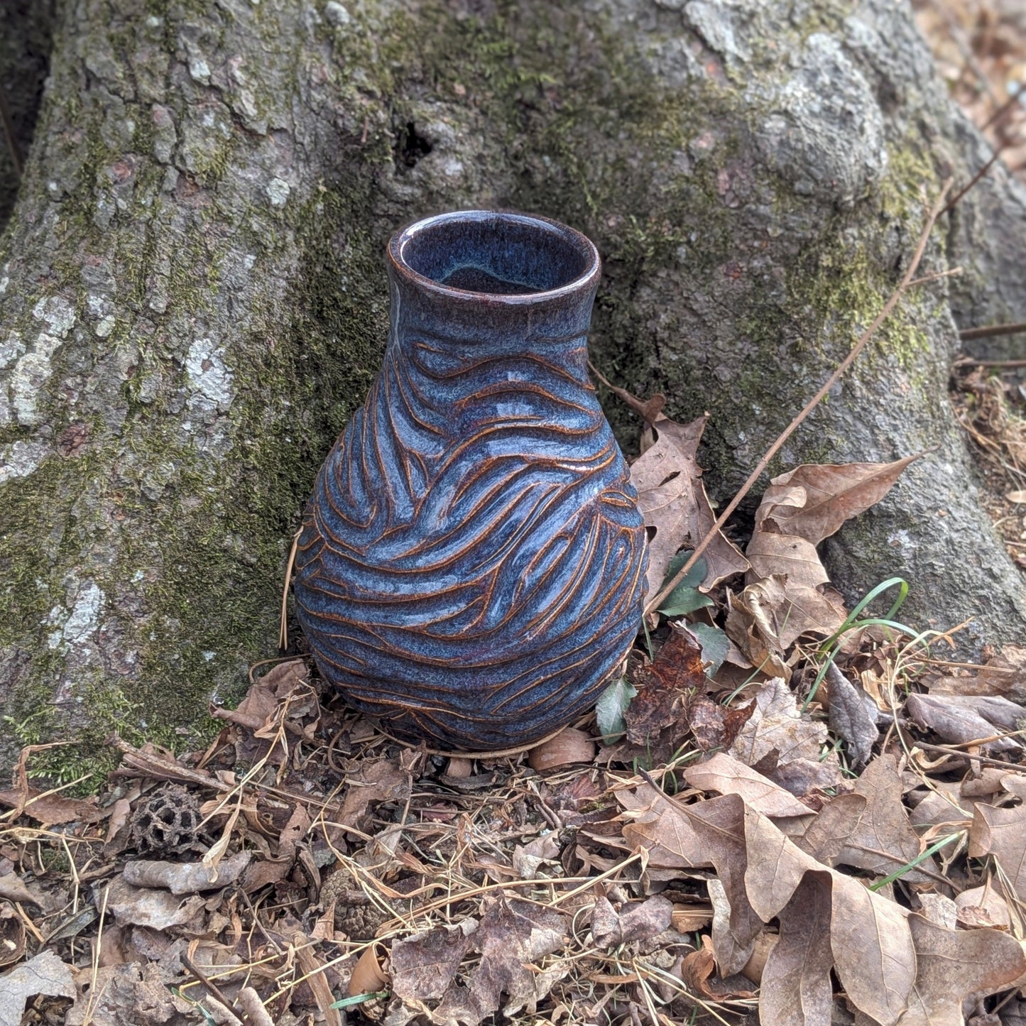 Ceramic vase with textured design on a forest floor with tree and leaves