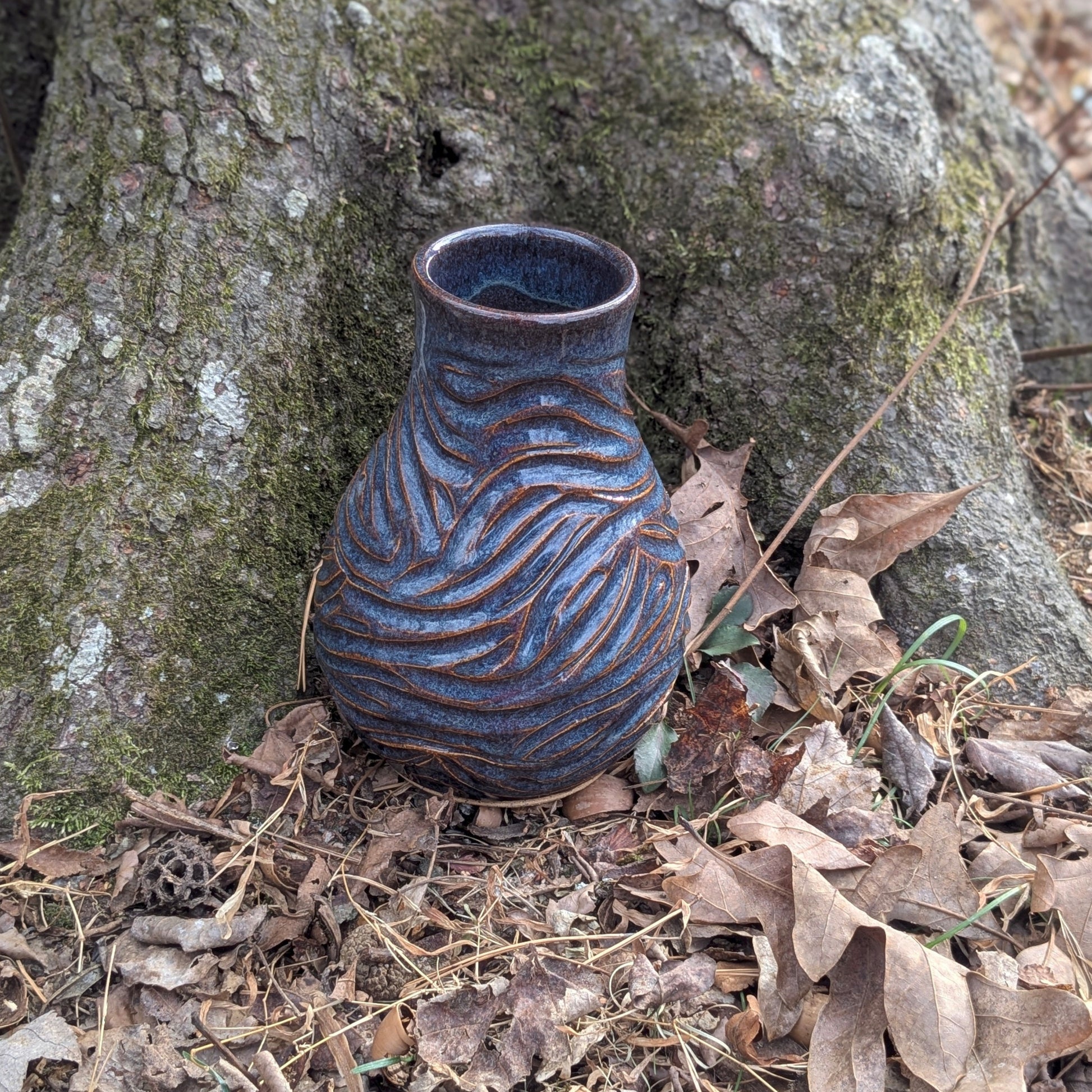 Ceramic vase with textured design on a forest floor with tree and leaves