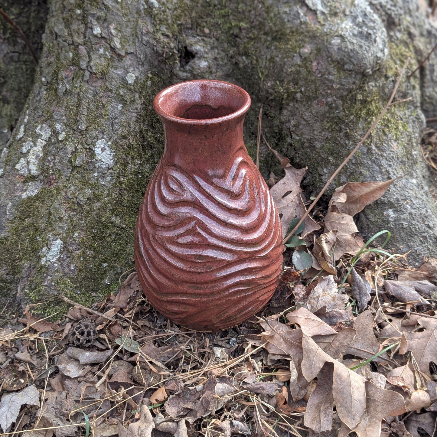 Ceramic vase with textured design on a forest floor with tree and leaves