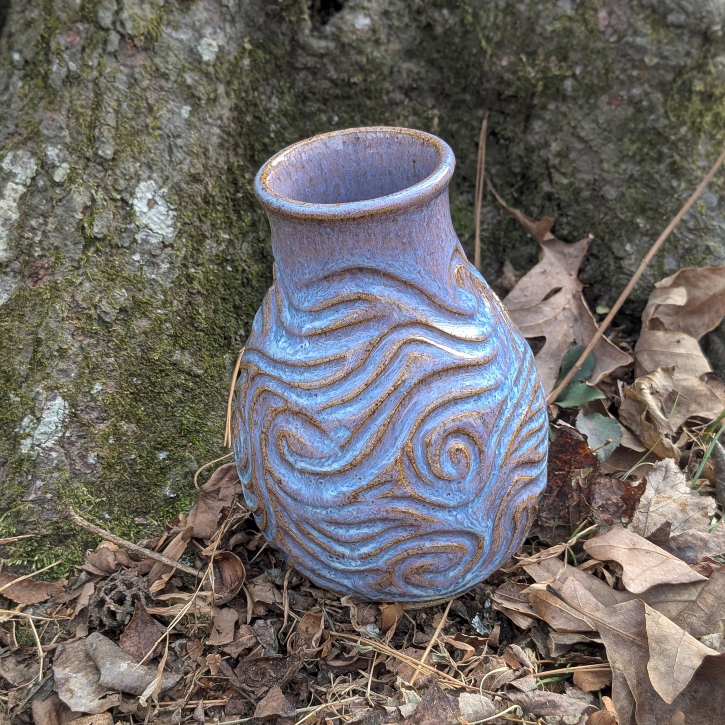 Ceramic vase with textured design on a forest floor with tree and leaves