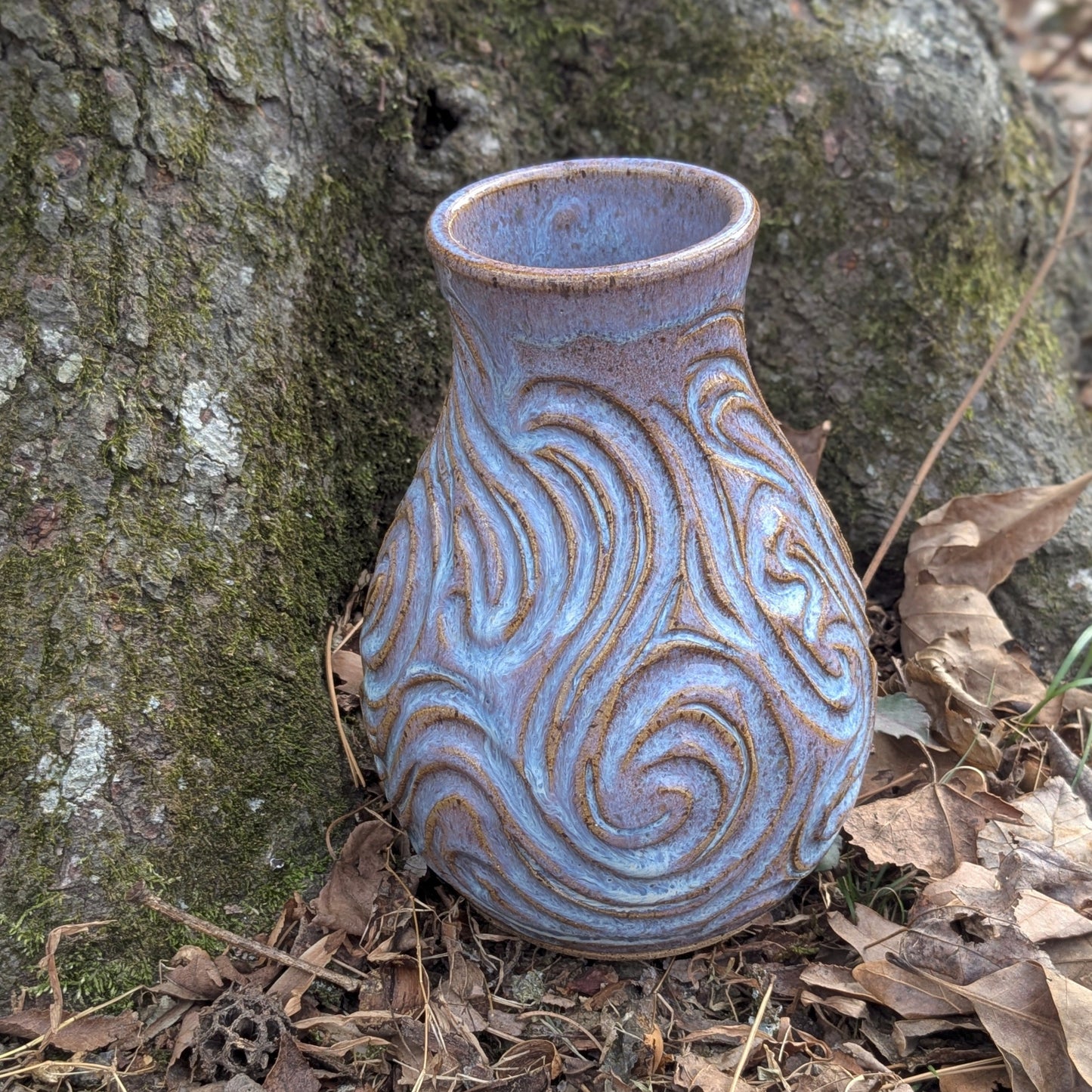 Ceramic vase with textured design on a forest floor with tree and leaves