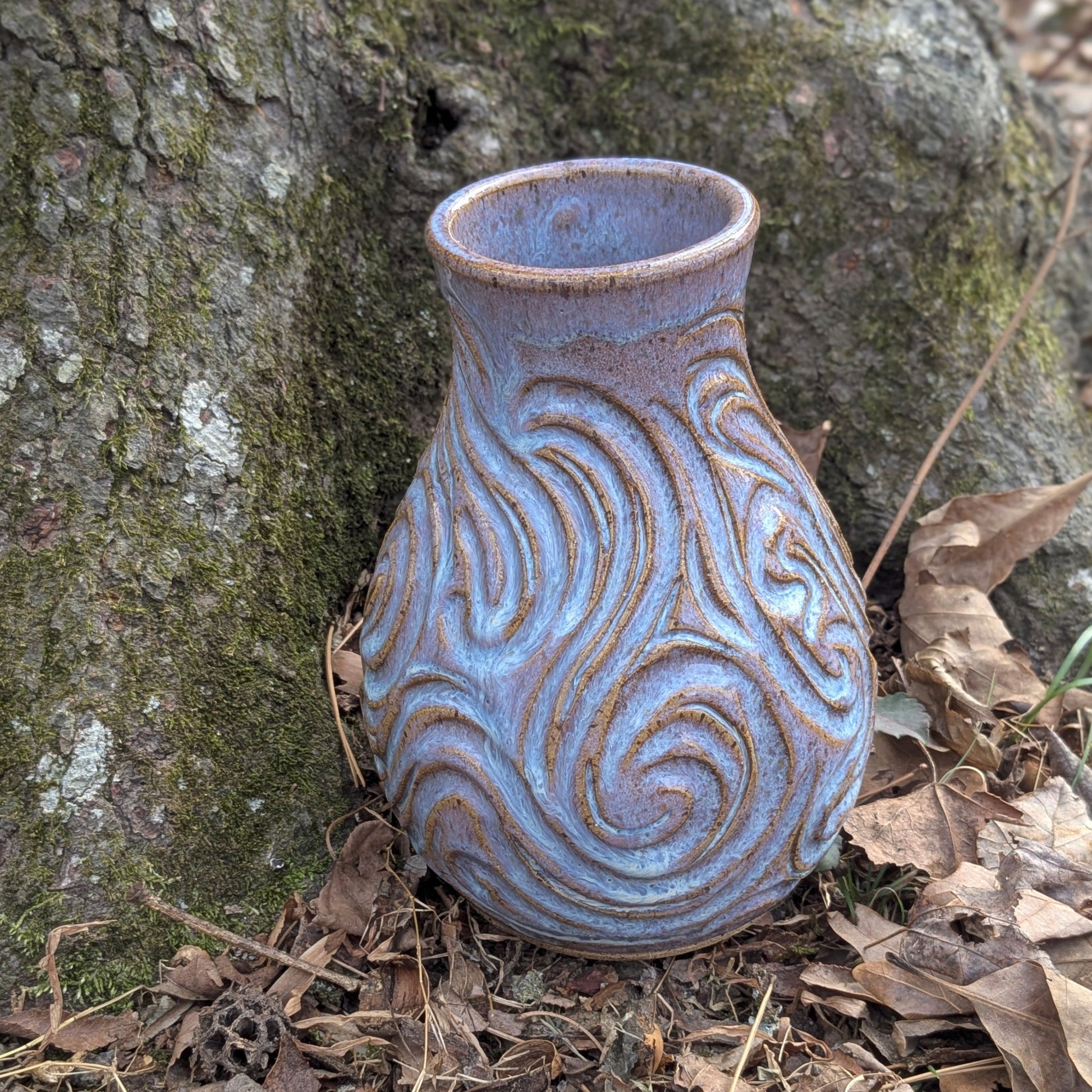 Ceramic vase with textured design on a forest floor with tree and leaves