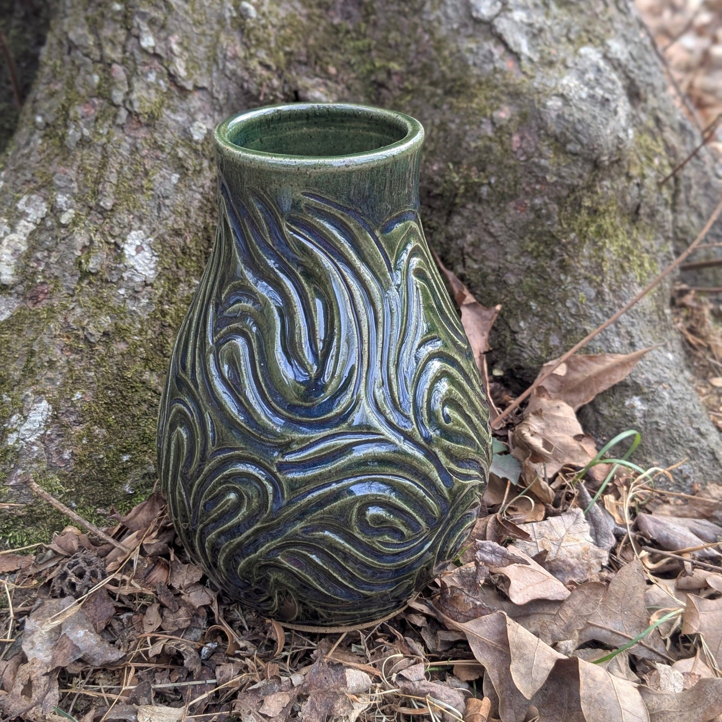 Ceramic vase with textured design on a forest floor with tree and leaves