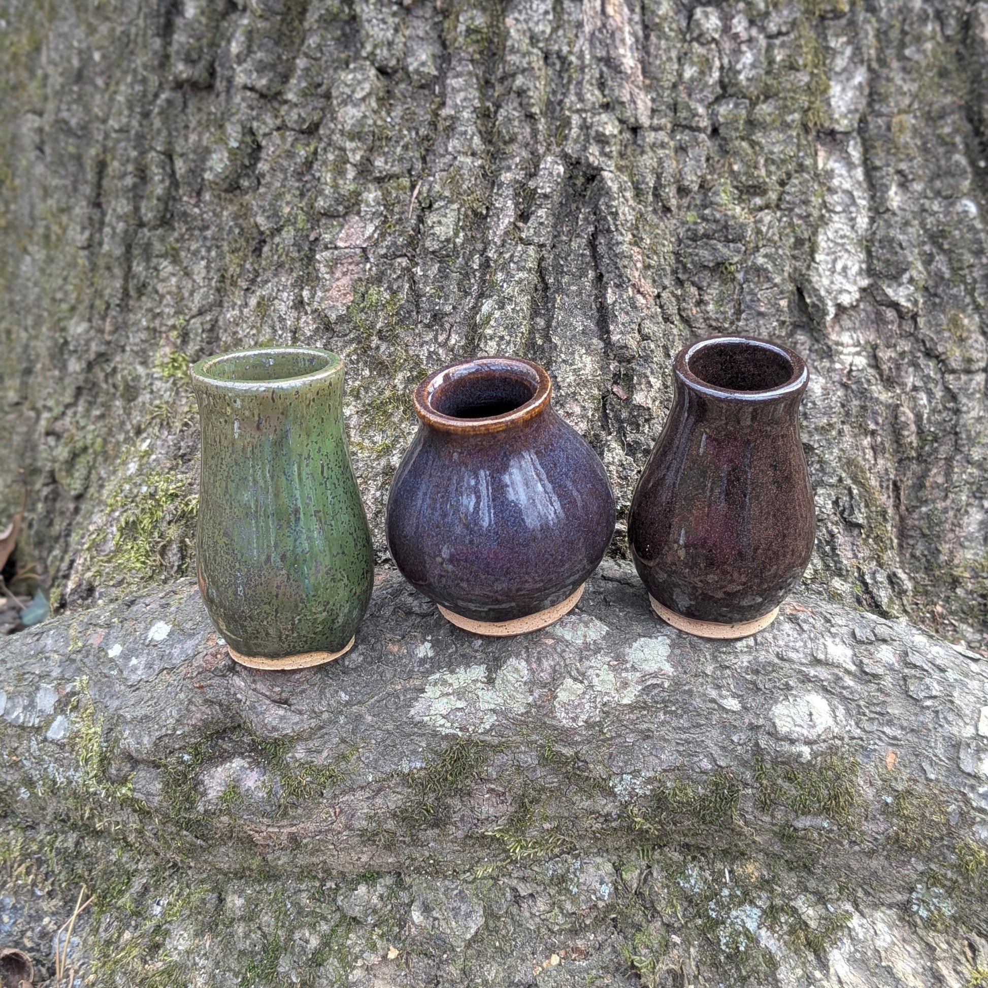 Three ceramic vases of different colors (green, purple, brown) on a tree stump.
