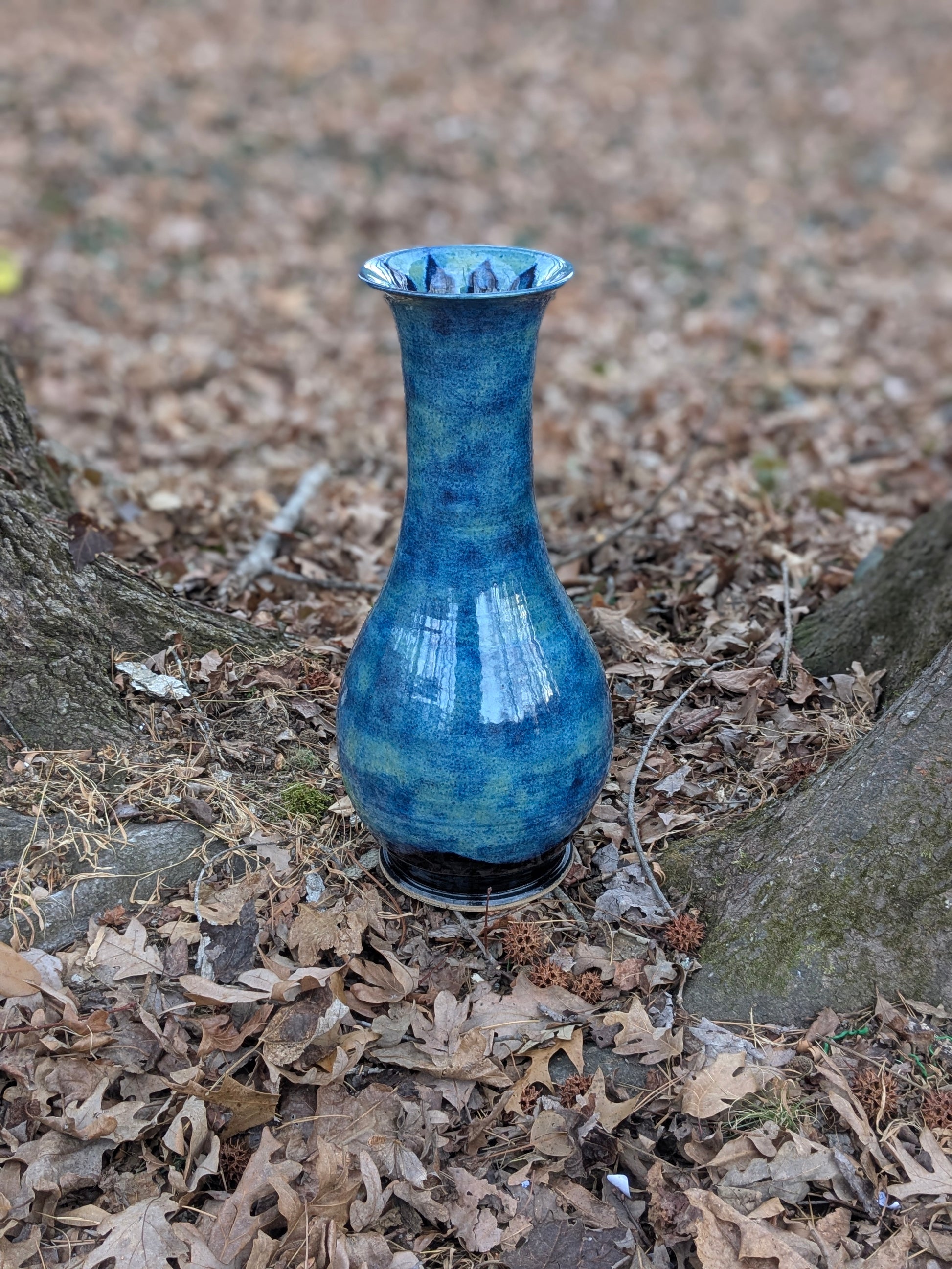 Blue ceramic vase on a bed of dry leaves and twigs.